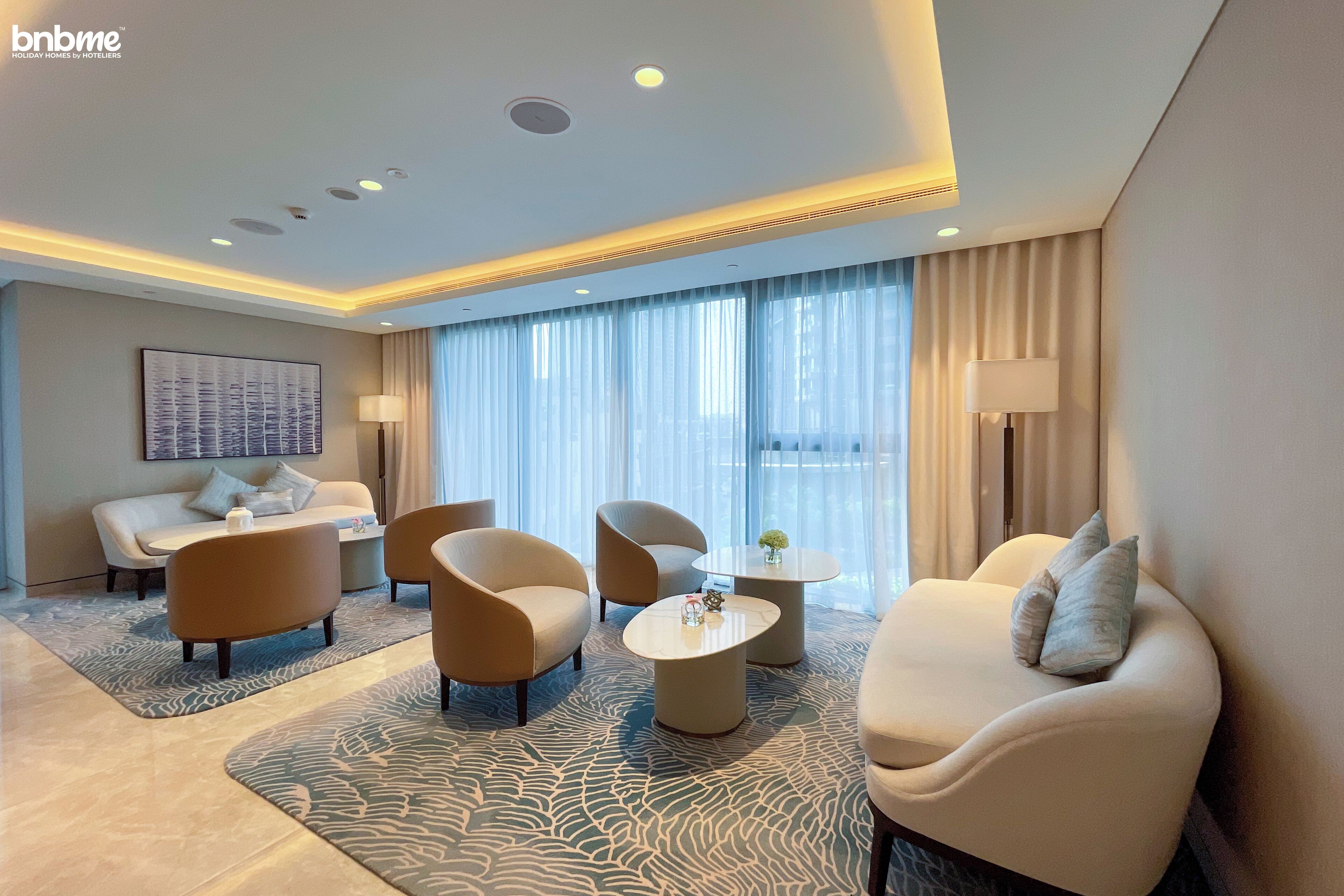 Habitación de hotel moderna con sofá, dos sillones, una mesita de café y un ventanal con cortinas.