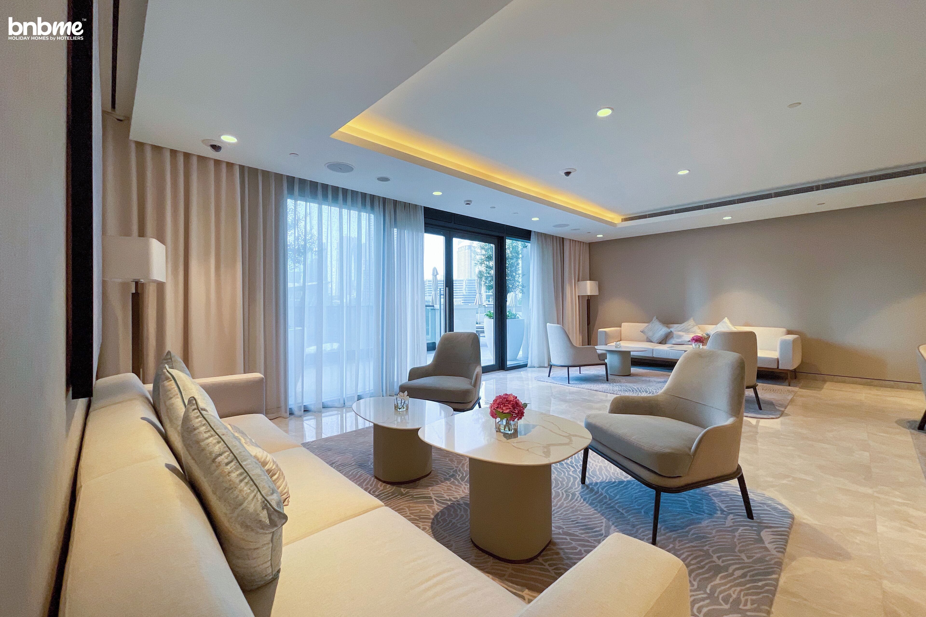 Une chambre d’hôtel moderne, dotée d’un grand canapé, de deux fauteuils, d’une table basse et offrant une vue sur la ville grâce à de grandes fenêtres.