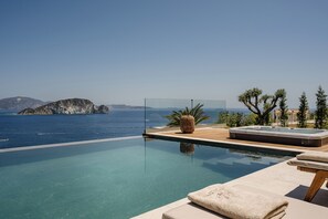 A clear view of a swimming pool with a hot tub and lounge area, overlooking a body of water and distant landforms. - Avgi Villa (Zakynthos)