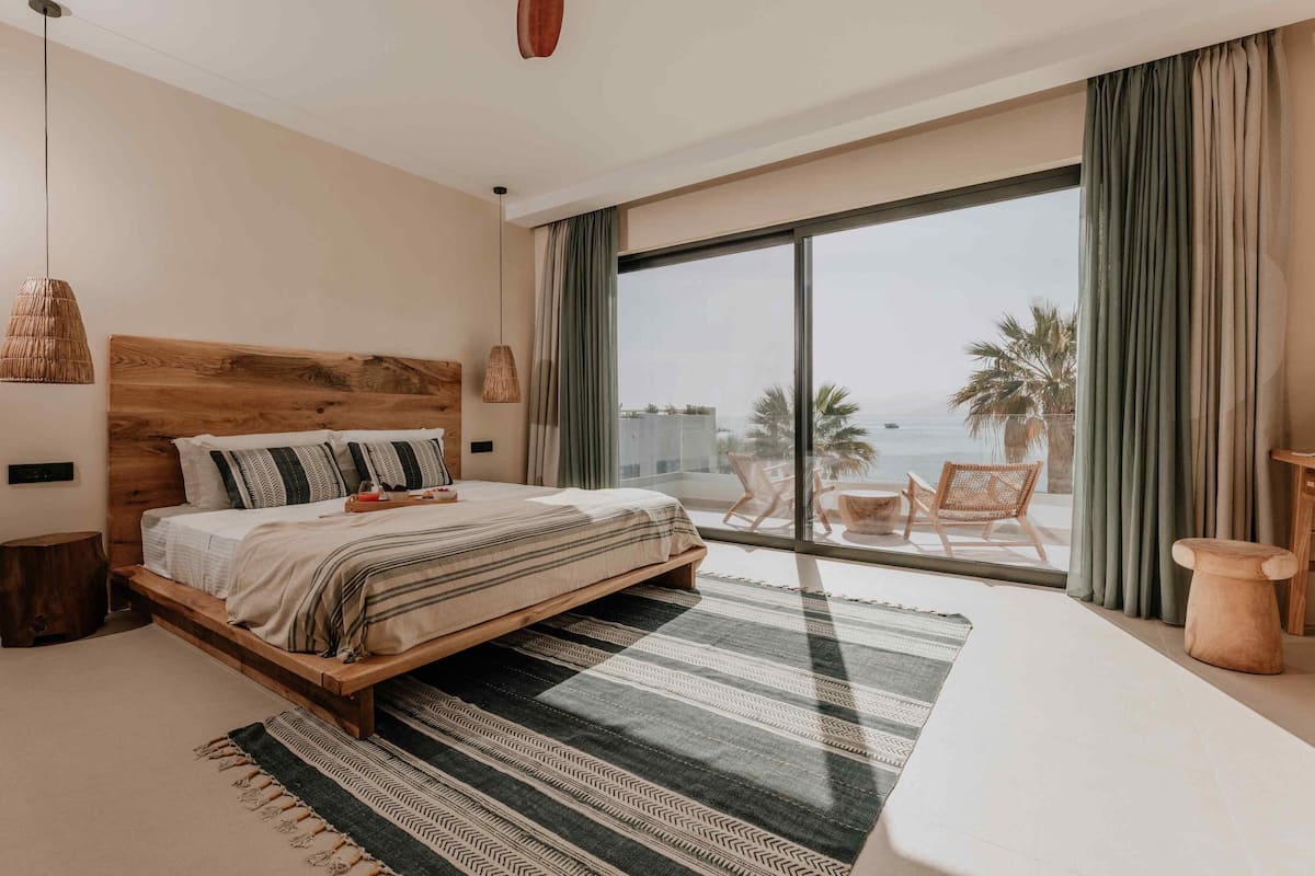 A bedroom with a large bed, a view of the sea, and a balcony with outdoor furniture.