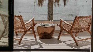 A balcony with two wicker chairs, a wooden table, and a large potted plant. - Ostrako Beachside Suites (Naxos)