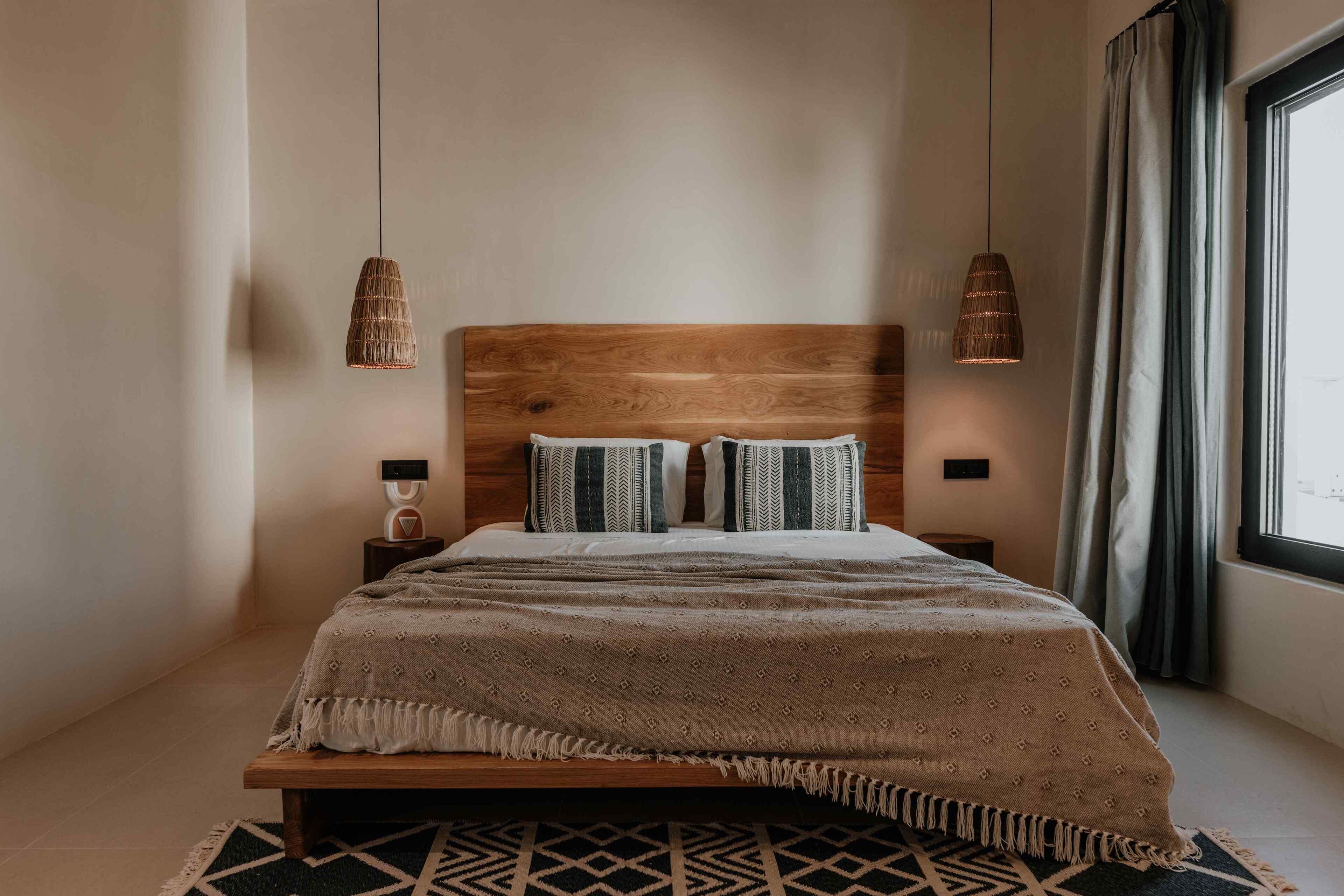 Un dormitorio moderno con cabecera de madera, colcha estampada y dos lámparas colgantes.