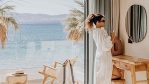 A room with a large window, a wooden desk, a chair, and a mirror. - Ostrako Beachside Suites (Naxos)