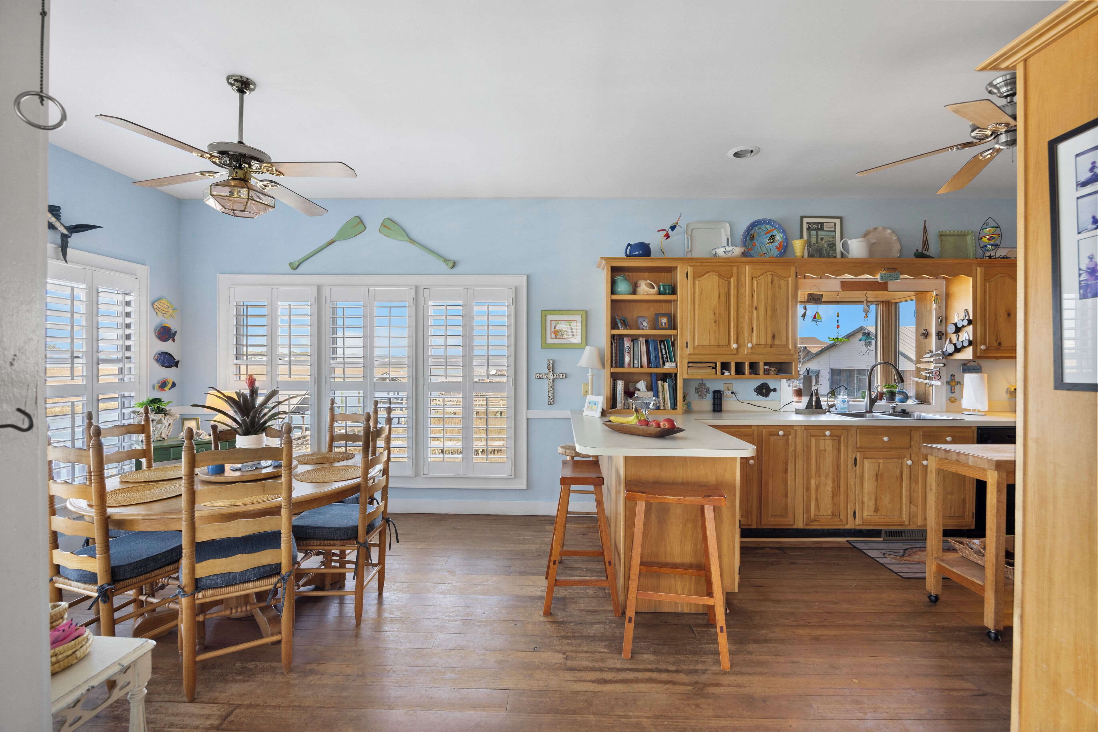 A kitchen with wooden cabinets, a dining area with striped chairs, and a view of the outside through large windows.