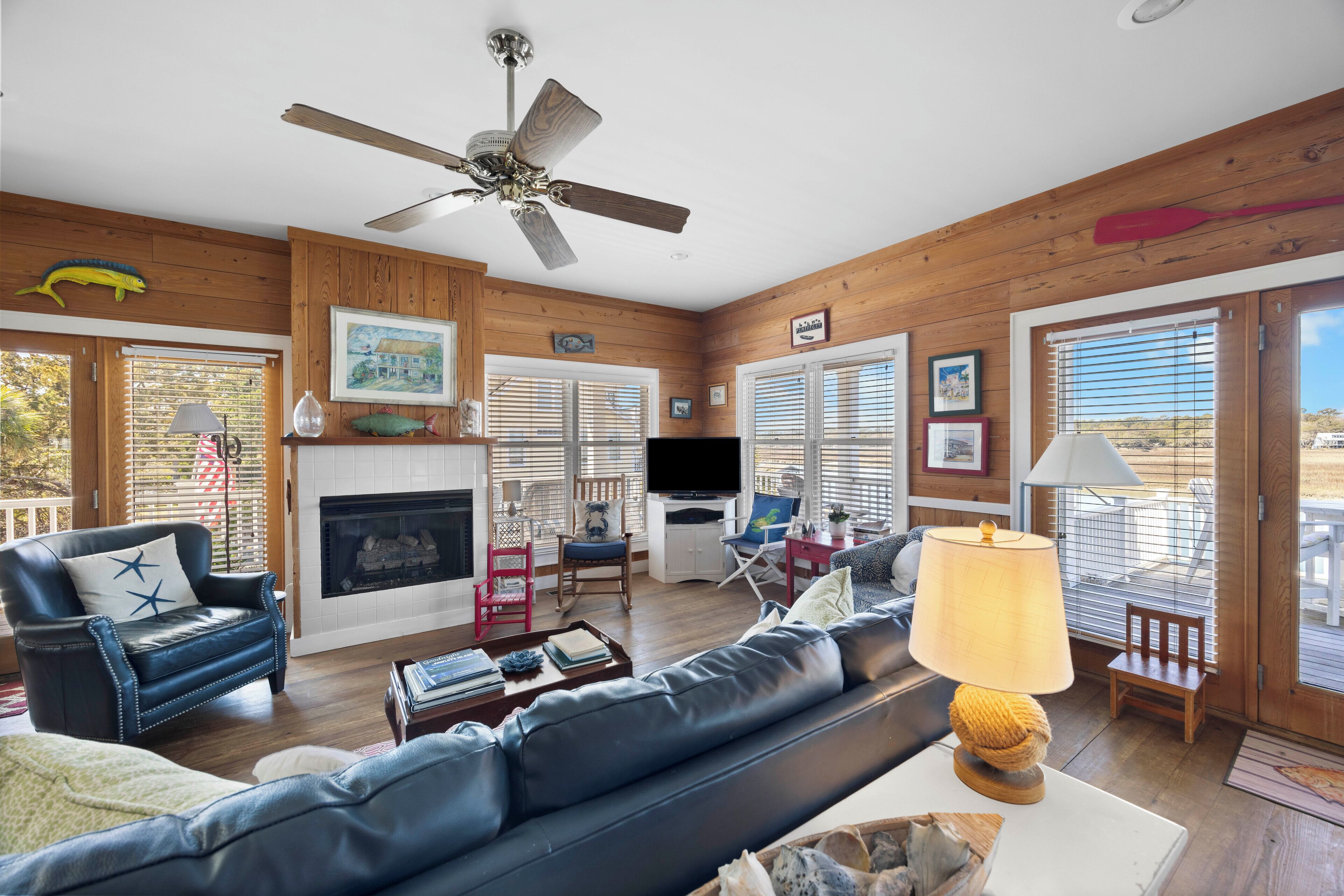 A cozy living room with a fireplace, leather sofa, and a ceiling fan.