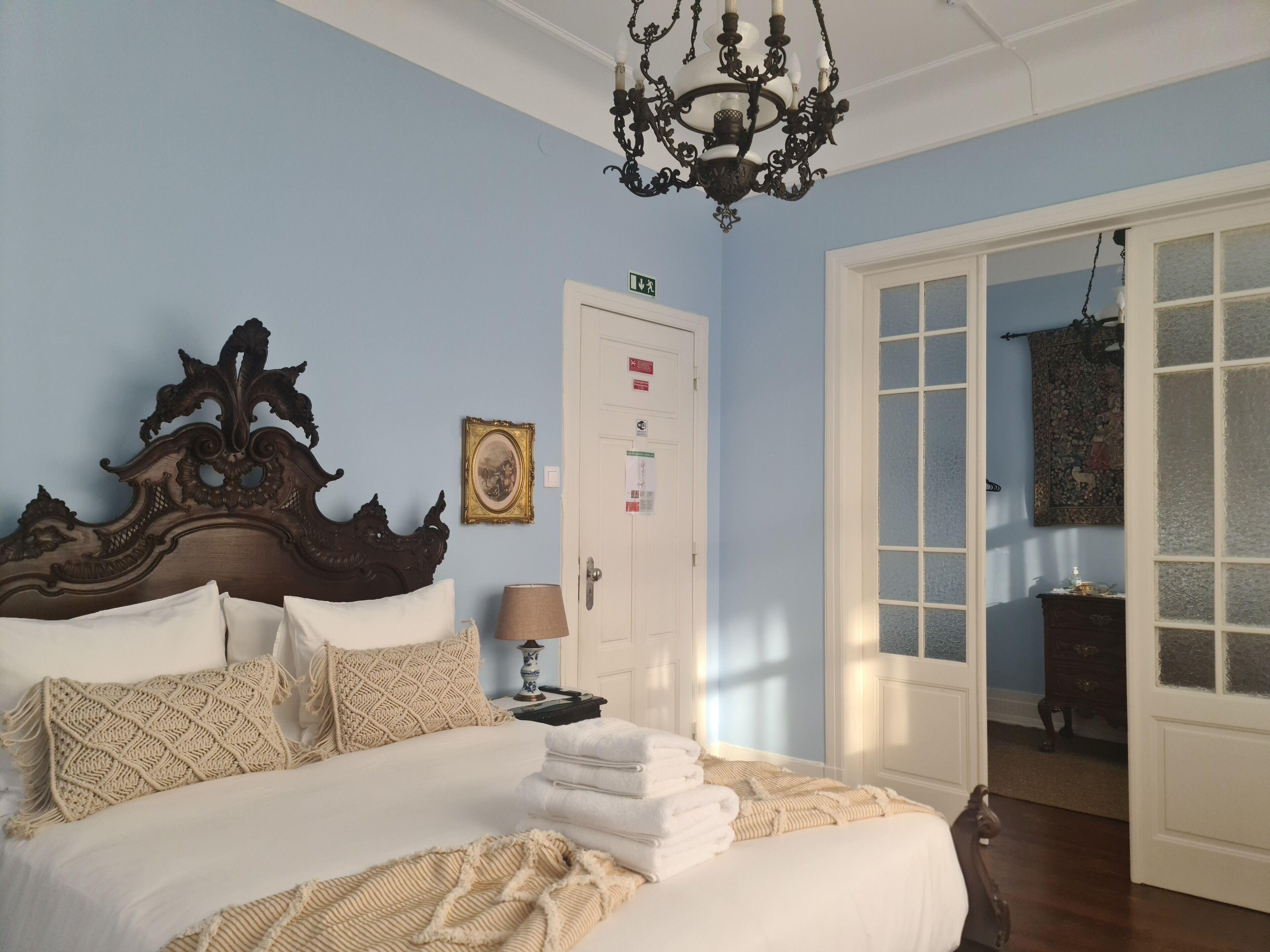 A bedroom with a large bed, a chandelier, a door with a sign, and a view through a glass door.