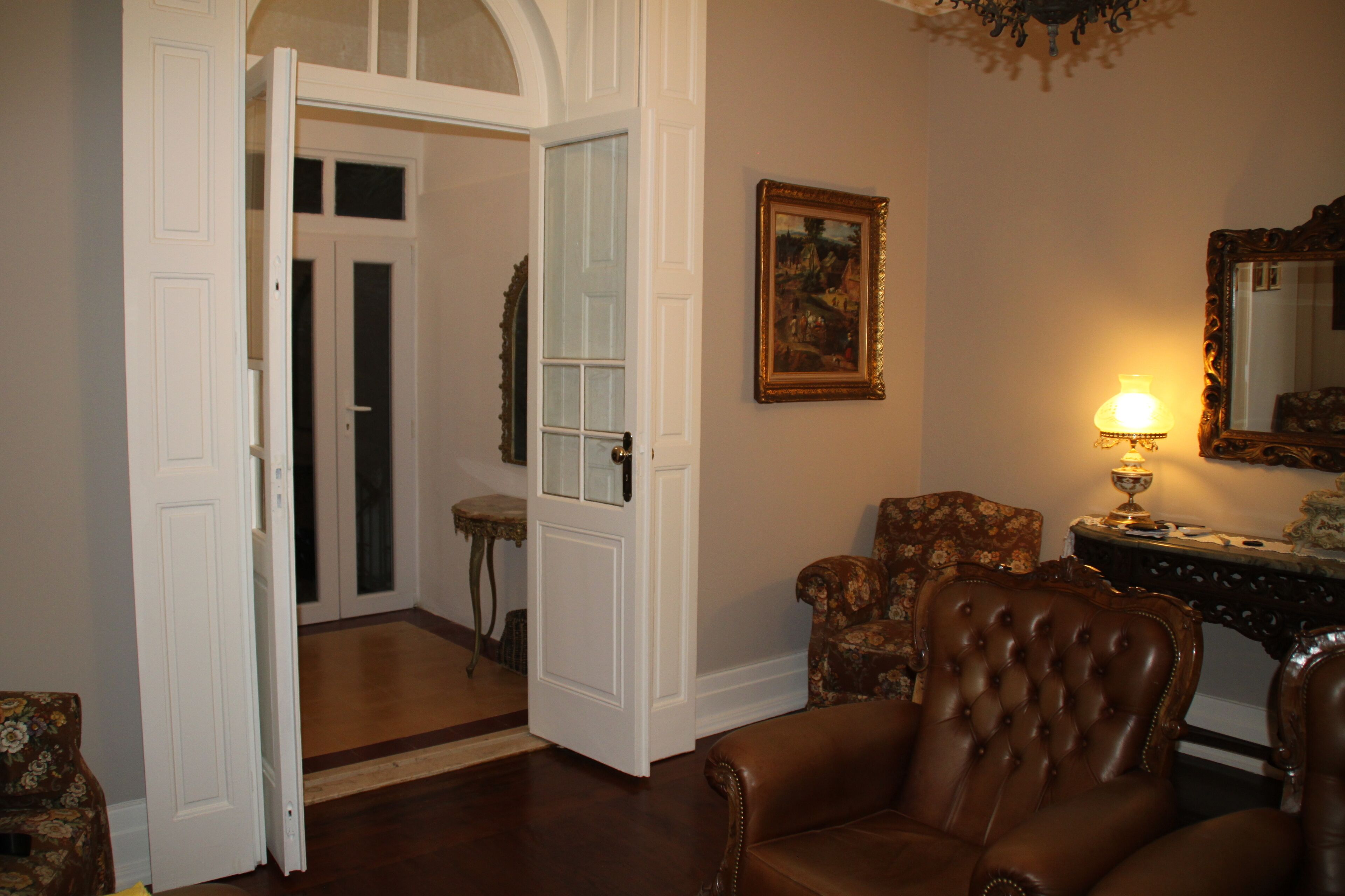 Una habitación con un sillón de cuero marrón, una puerta de madera, una mesita y una lámpara.