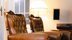 A room with two brown leather chairs with tufted backs, a lamp, and a piano.