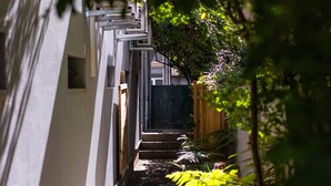 A narrow pathway flanked by greenery and a building facade.