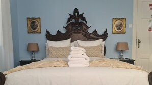 A neatly made bed with a large pile of folded towels, two bedside tables with lamps, and two framed pictures on the wall.