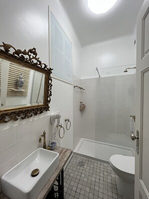 Une salle de bain avec un lavabo blanc, un miroir doté d’un cadre orné, un espace douche et des toilettes.
