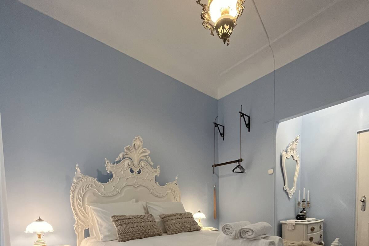 Une chambre à coucher avec un grand lit, une table de chevet, une lampe, un luminaire suspendu, un miroir et une porte.