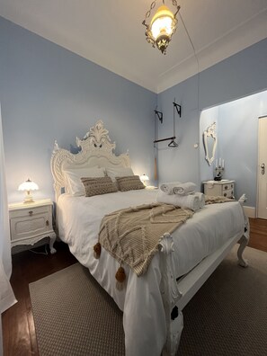 Une chambre à coucher avec un grand lit, une table de chevet, une lampe, un luminaire suspendu, un miroir et une porte.