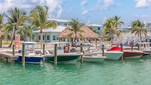A marina with several boats docked, a thatched-roof structure, and a row of buildings with a white facade. - Ocean Isles #98~ Fishing Village, Community Pool! (Marathon)