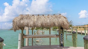 A wooden dock with a thatched roof structure, leading into a calm body of water. - Ocean Isles #98~ Fishing Village, Community Pool! (Marathon)