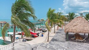 A beachside resort with thatched-roof structures, lounge chairs, and boats docked by the water. - Ocean Isles #98~ Fishing Village, Community Pool! (Marathon)