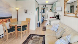 Ein gemütliches Wohnzimmer mit Sofa, einem Esstisch mit Stühlen, einer Küchenzeile mit Mikrowelle und einem Flur, der in einen anderen Raum führt.