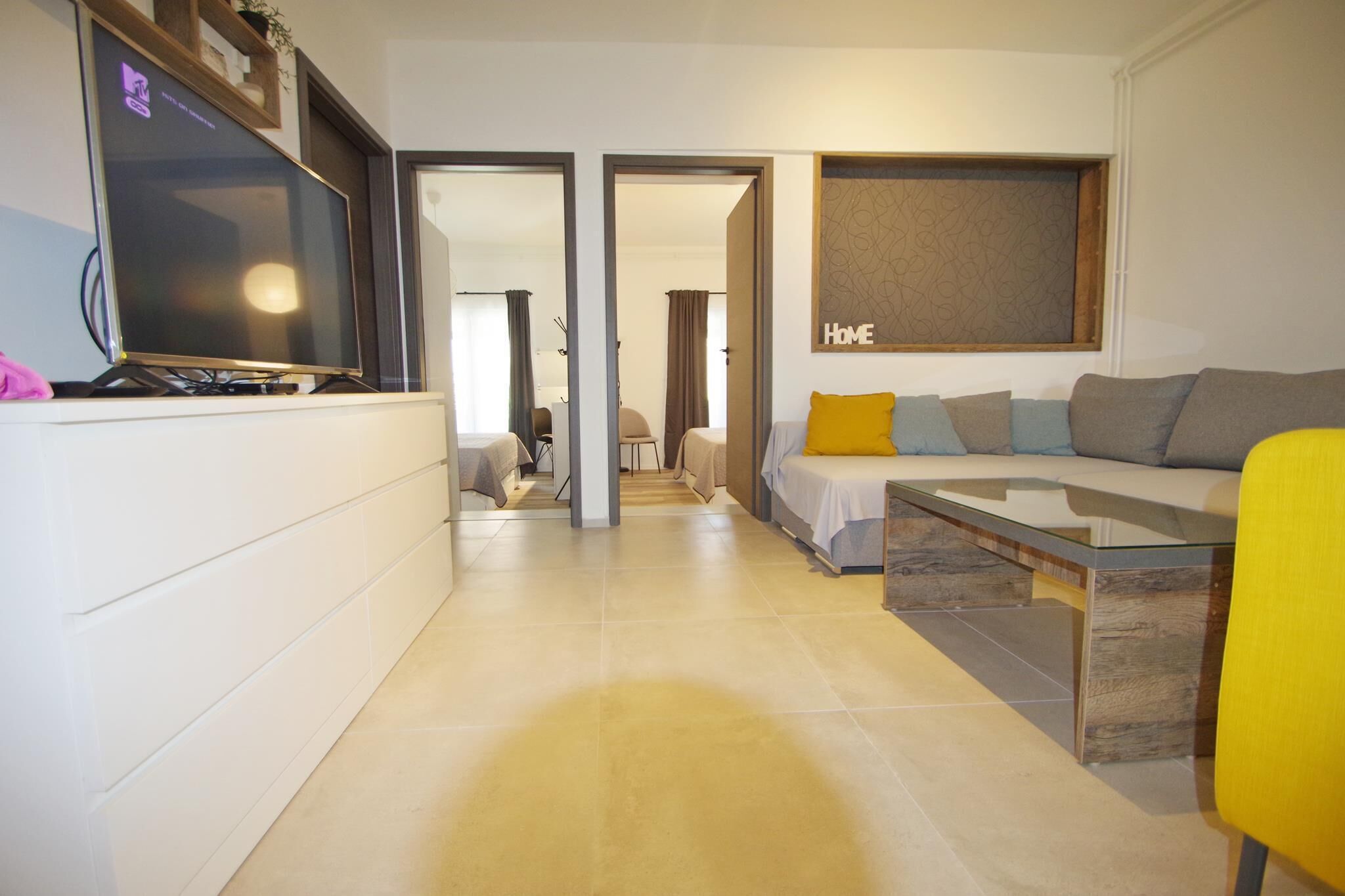 A modern living room with a sofa, coffee table, and television. There is a hallway leading to another room.