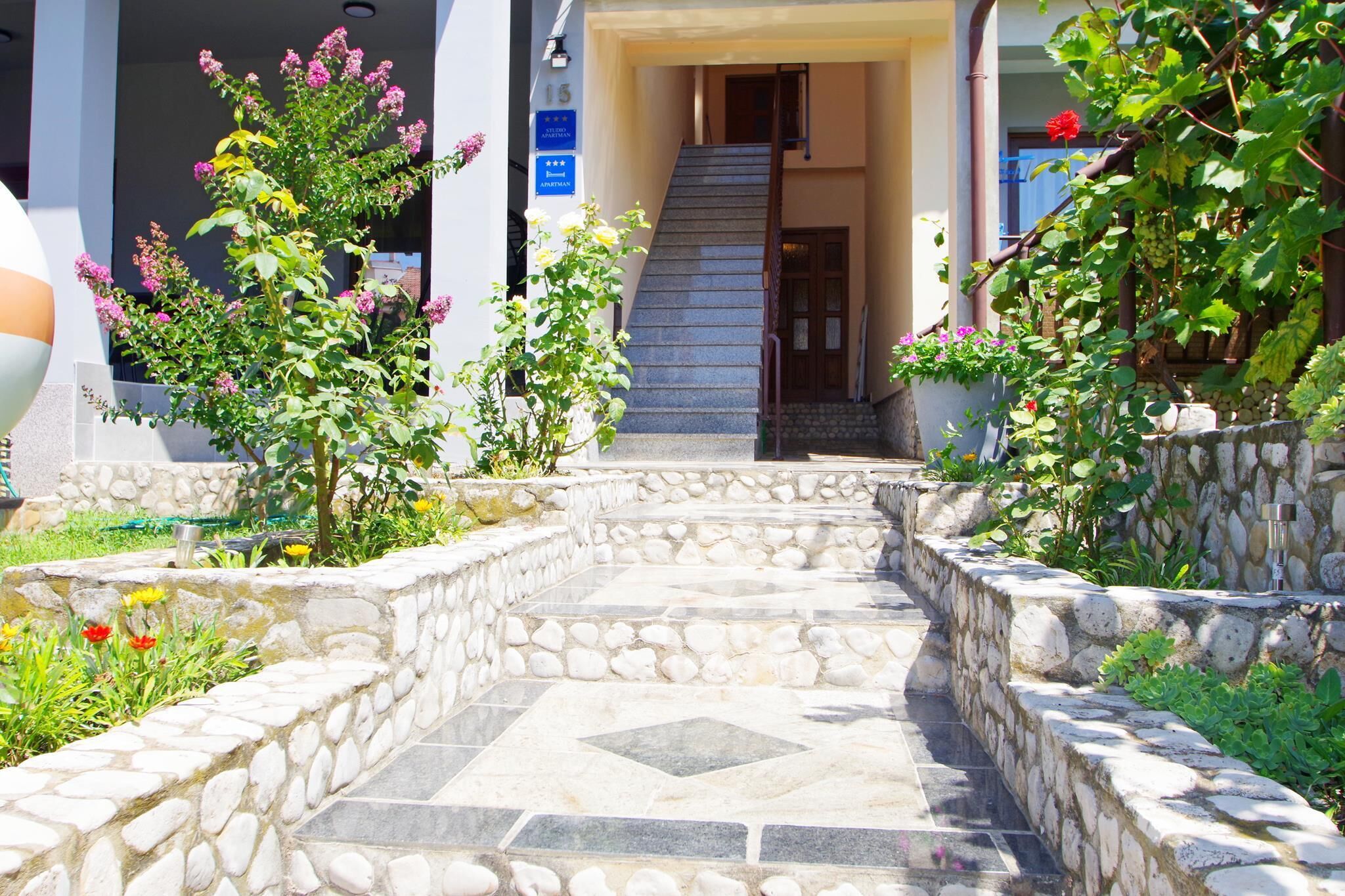 Una escalera de piedra conduce a la entrada de un edificio, rodeado de follaje y flores.