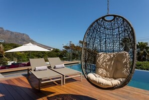 Een zwembadterras met een hangstoel, ligbedden en een parasol.