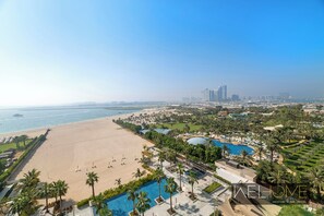 Relax on a large sandy beach adjacent to a clear sea, surrounded by lush greenery and palm trees.
