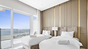 Enjoy a beach and city view from the large balcony, featuring a comfortable bed and a stylish bedside table.