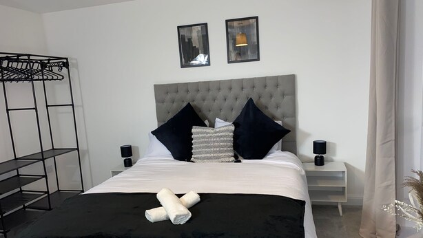 A neatly arranged bedroom with a bed, two bedside tables, a hanging light fixture, and a wall-mounted shelf. - Family Home 5-bed House in Birmingham City Centre (Birmingham)