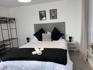 Una camera da letto ordinata con un letto, due comodini, una lampada a sospensione e una mensola a parete.