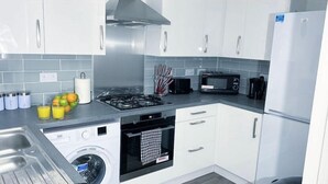 A modern kitchen with white cabinets, a stainless steel range hood, a microwave, a toaster, and a washing machine. - Family Home 5-bed House in Birmingham City Centre (Birmingham)