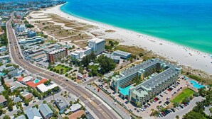 An aerial view of a coastal city with a beachfront hotel, roads, and surrounding buildings.