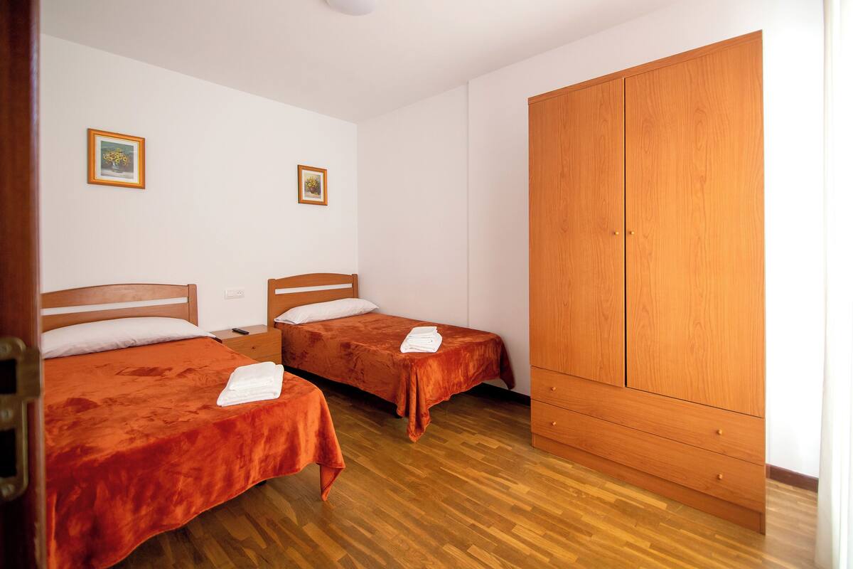 Una habitación con dos camas, un armario de madera y dos cuadros en la pared.