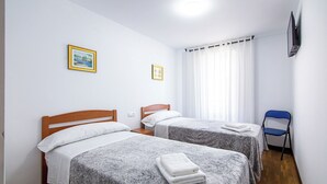 A room with two beds, a chair, a TV, and a window with curtains. - Yani's hospedaje (Parres)
