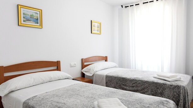 A hotel room with two single beds, a wooden headboard, white bedding, and a window with white curtains. - Yani's hospedaje (Parres)