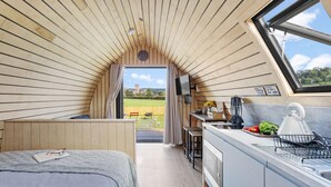 A compact, modern room with a sloped ceiling, a small kitchenette, a bed, and a view of a green landscape through a window. - The West Front, Cathedral View - Hot Tub - Pets - Free Parking & WiFi (Wells)