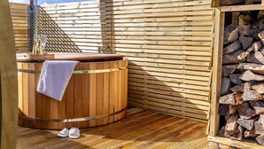 A wooden sauna with a towel and slippers on the floor, a wooden bench, and a stack of firewood. - The West Front, Cathedral View - Hot Tub - Pets - Free Parking & WiFi (Wells)