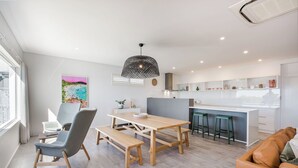 A modern kitchen with a central island, wooden dining table with benches, and a bar area with stools.