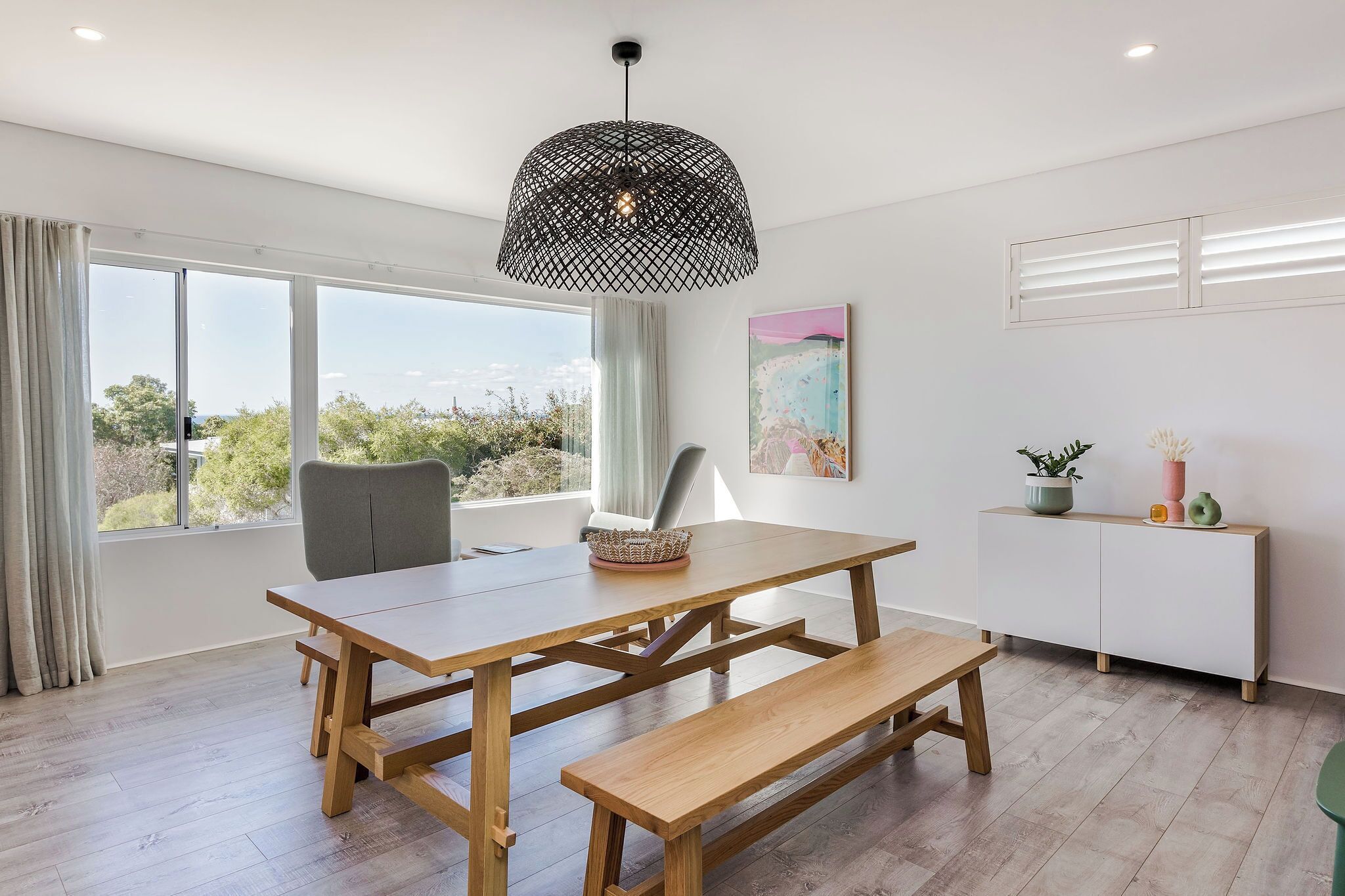 A modern dining area with a wooden table, bench, and pendant light.