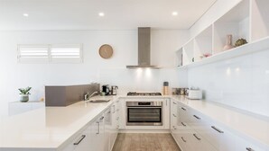 A modern kitchen with white cabinetry, a built-in oven, a stainless steel range hood, and a large island with a sink.