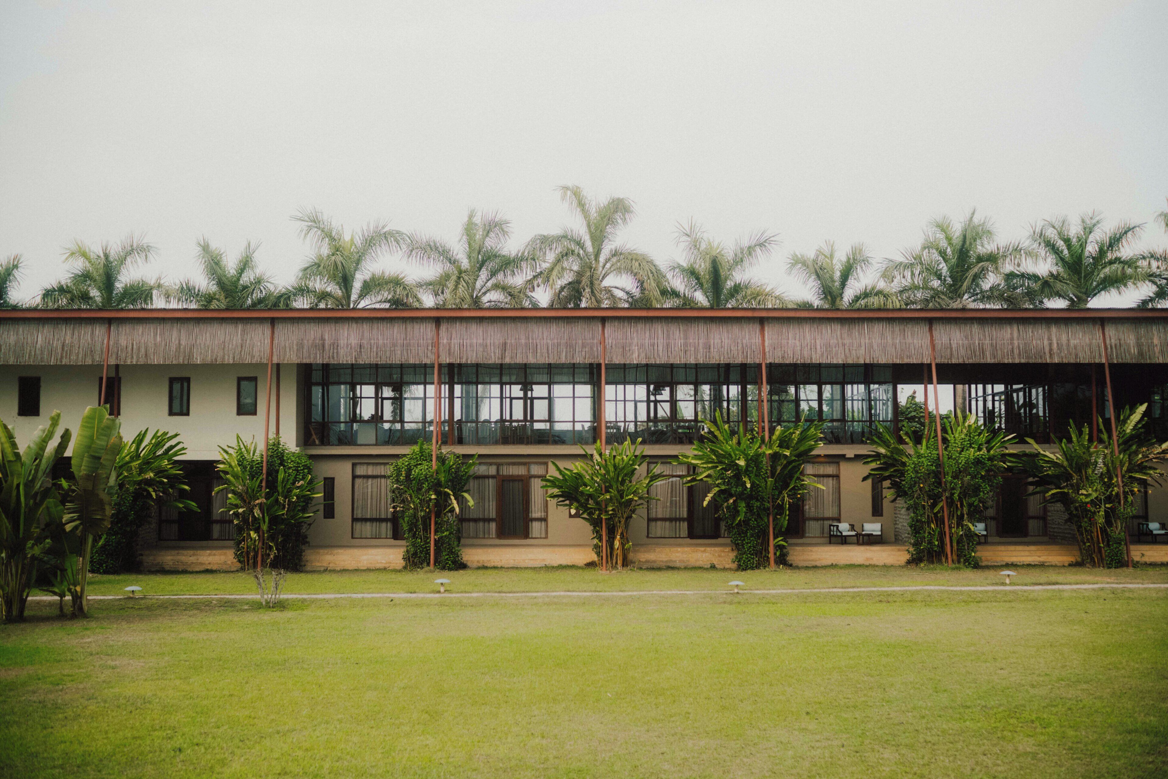 A building with a thatched roof, large windows, and a lawn with palm trees.