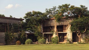 A two-story building with a balcony, surrounded by lush greenery and a well-maintained lawn.