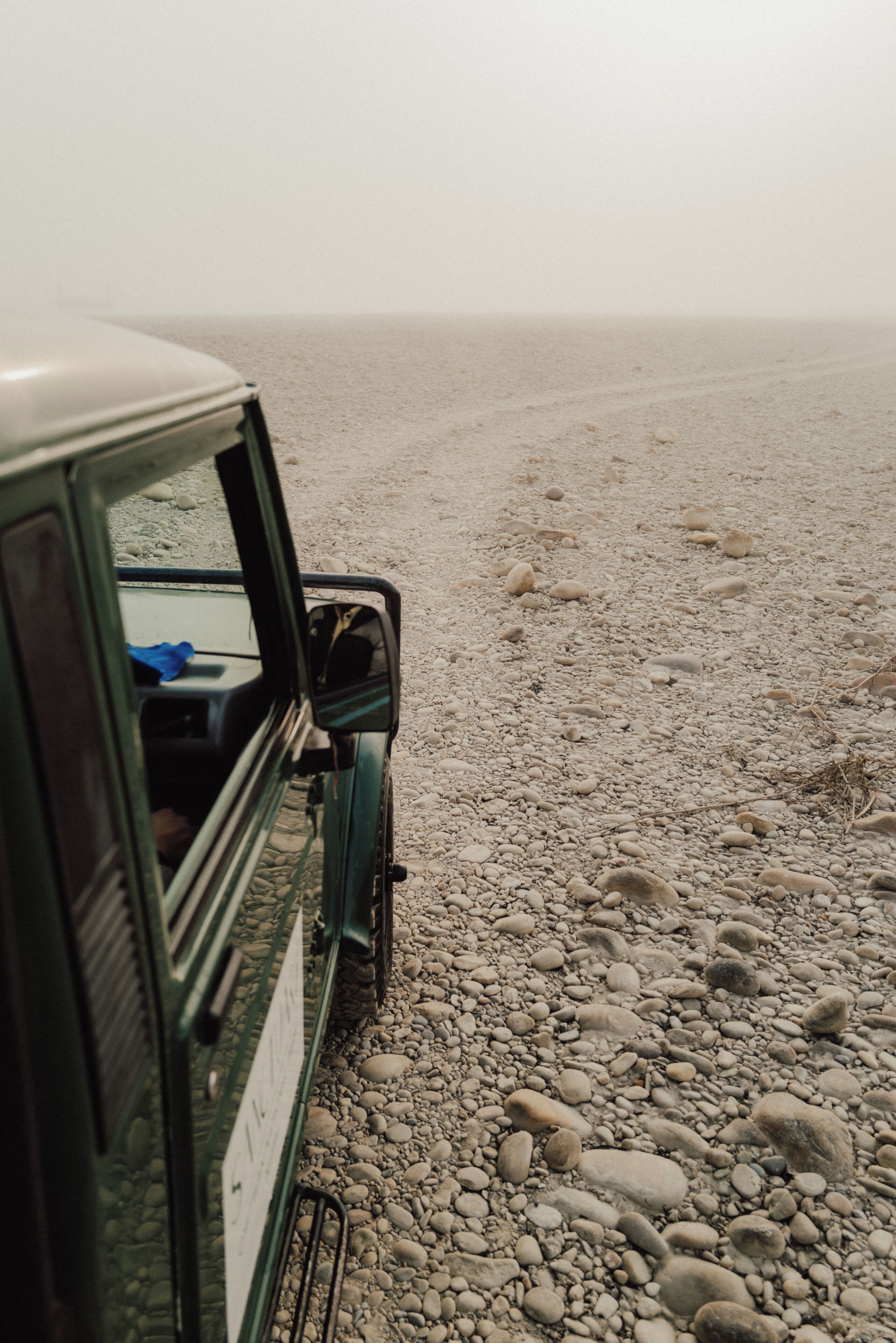 A vehicle parked on a gravel surface with a view of the sea.