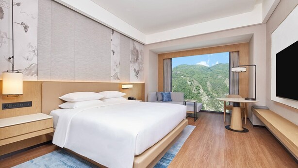 A modern hotel room with a large bed, a desk, a chair, and a TV. - Courtyard By Marriott Jiuzhaigou (Ngawa Autonomous Prefecture)