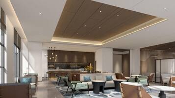 A spacious lounge area with a modern kitchen in the background, a seating area with sofas and tables, and a high ceiling with recessed lighting.