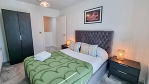 A bedroom with a bed, a nightstand, a wardrobe, and a framed picture on the wall. - 4 Bed Townhouse | Free Parking | Piccadilly (Greater Manchester)