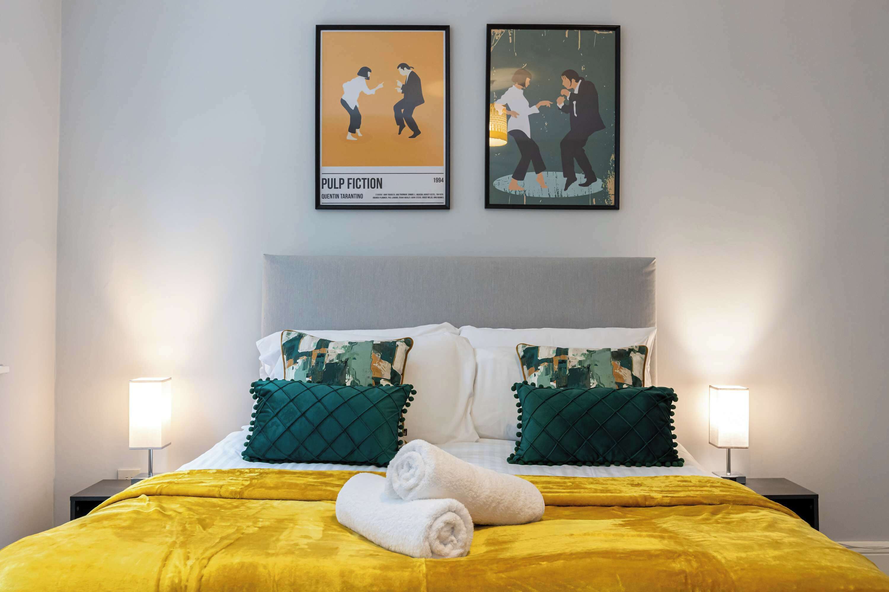 Une chambre d’hôtel avec un lit, deux oreillers, une serviette roulée et deux affiches encadrées accrochées au mur.