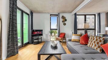 A modern living room with a flat-screen TV, a grey sofa, a coffee table, and a large window.
