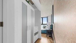 Ein Flur, der zu einem Schlafzimmer mit Bett, Schreibtisch und Fenster führt.
