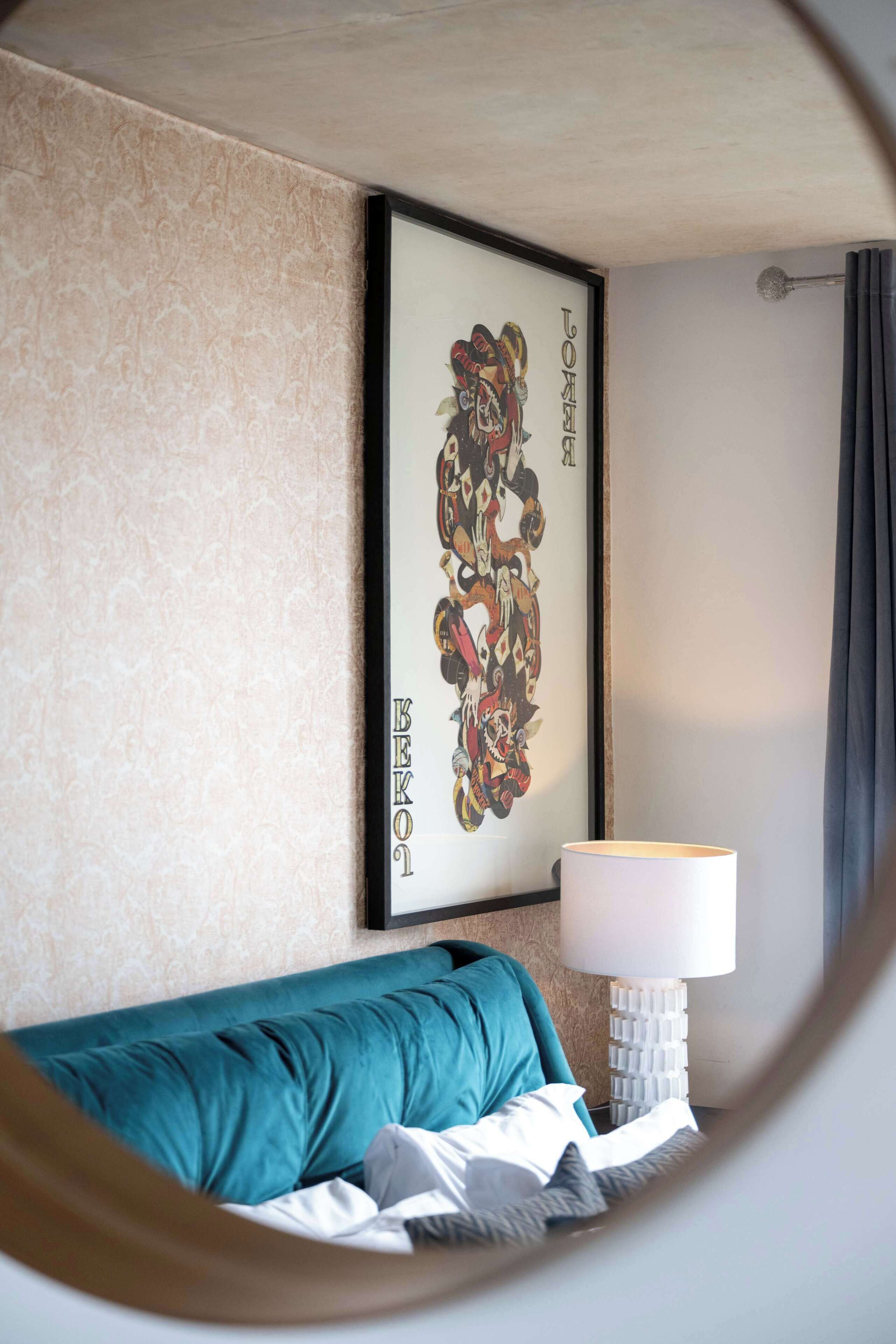 A room with a teal sofa, a framed artwork on the wall, and a lamp on a side table.