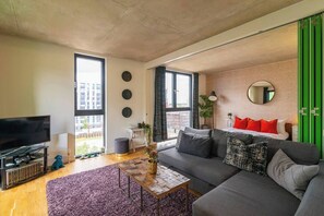 Uma sala de estar moderna com um sofá cinzento, uma televisão de tela plana, uma mesa de centro e uma janela grande.