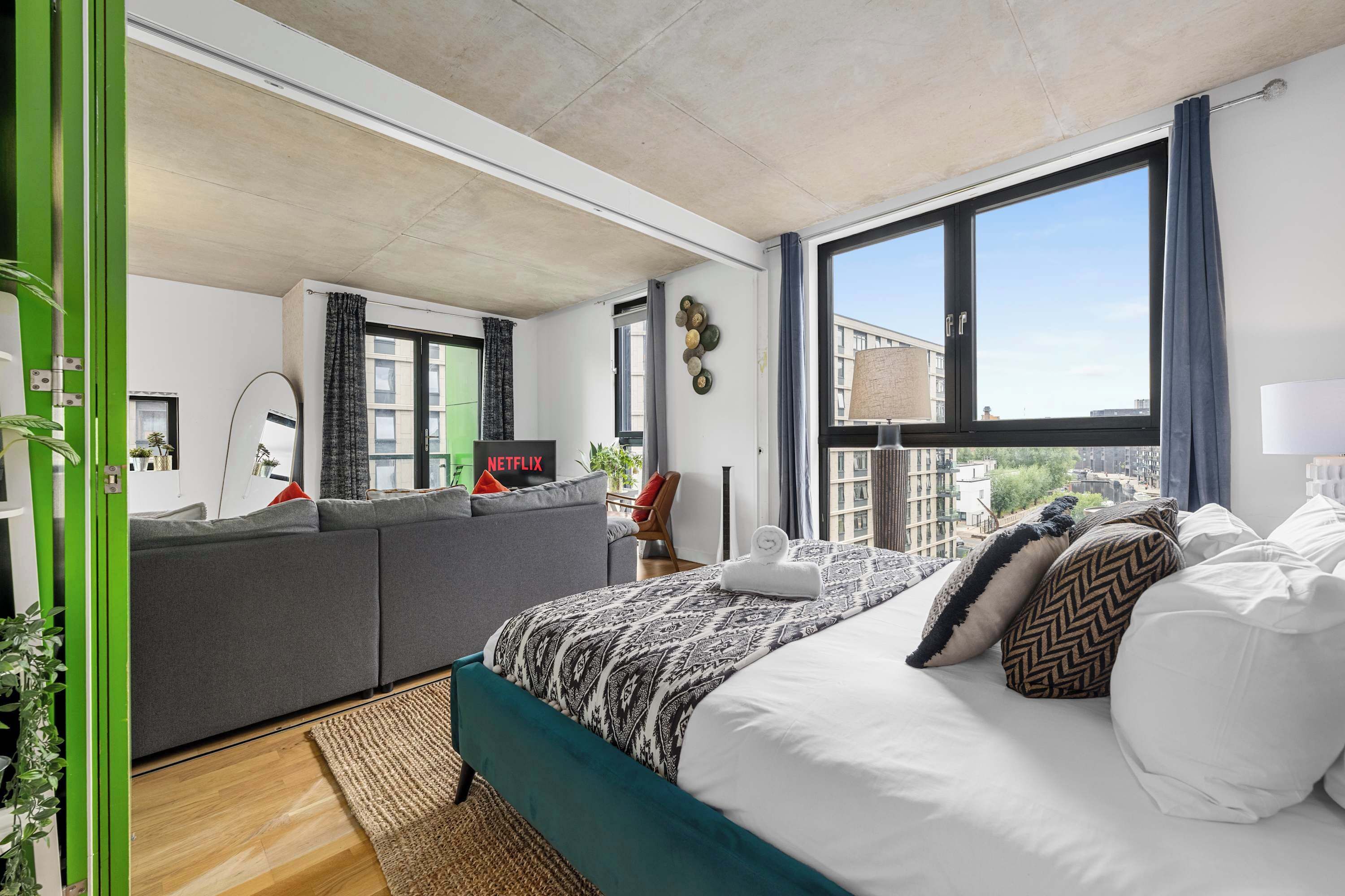 A modern bedroom with a large bed, a sofa, a view of the city, and a green door.
